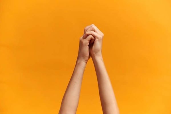 Arms and clasped hands on yellow orange bkgrd